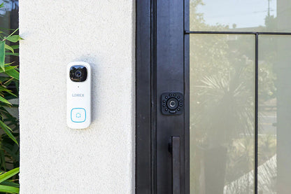 Smart doorbell attached to a house exterior next to a glass door.